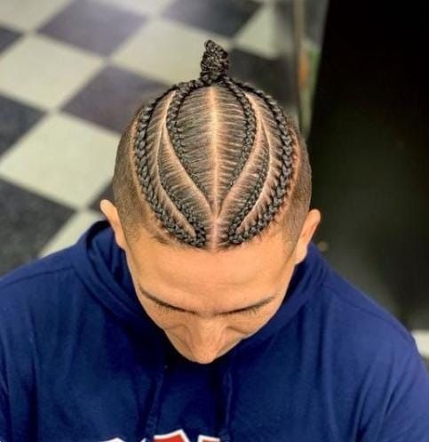 Primer plano de un hombre con peinado trenzado, con los lados rapados y un pequeño moño en la parte superior.