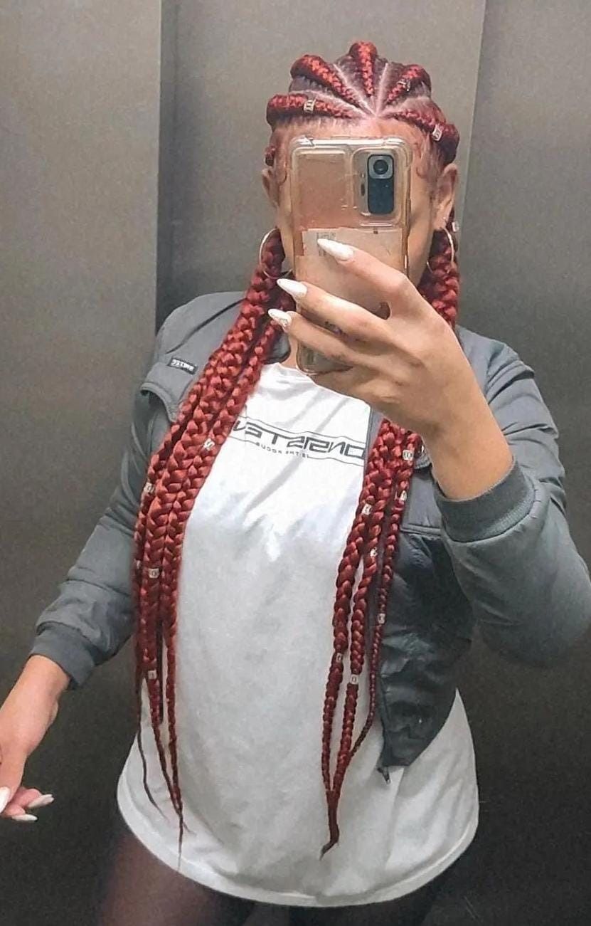 Persona con trenzas rojas se toma un selfie en un espejo, vistiendo una camisa blanca y una chaqueta negra.