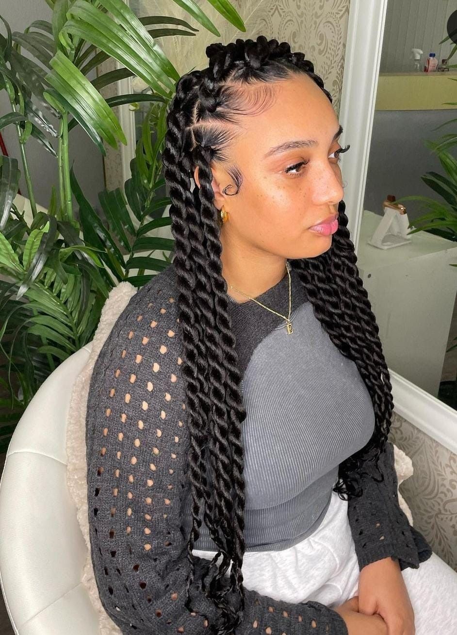 Mujer con largas trenzas negras, sentada en un interior. Lleva una blusa negra y pantalones cortos blancos.