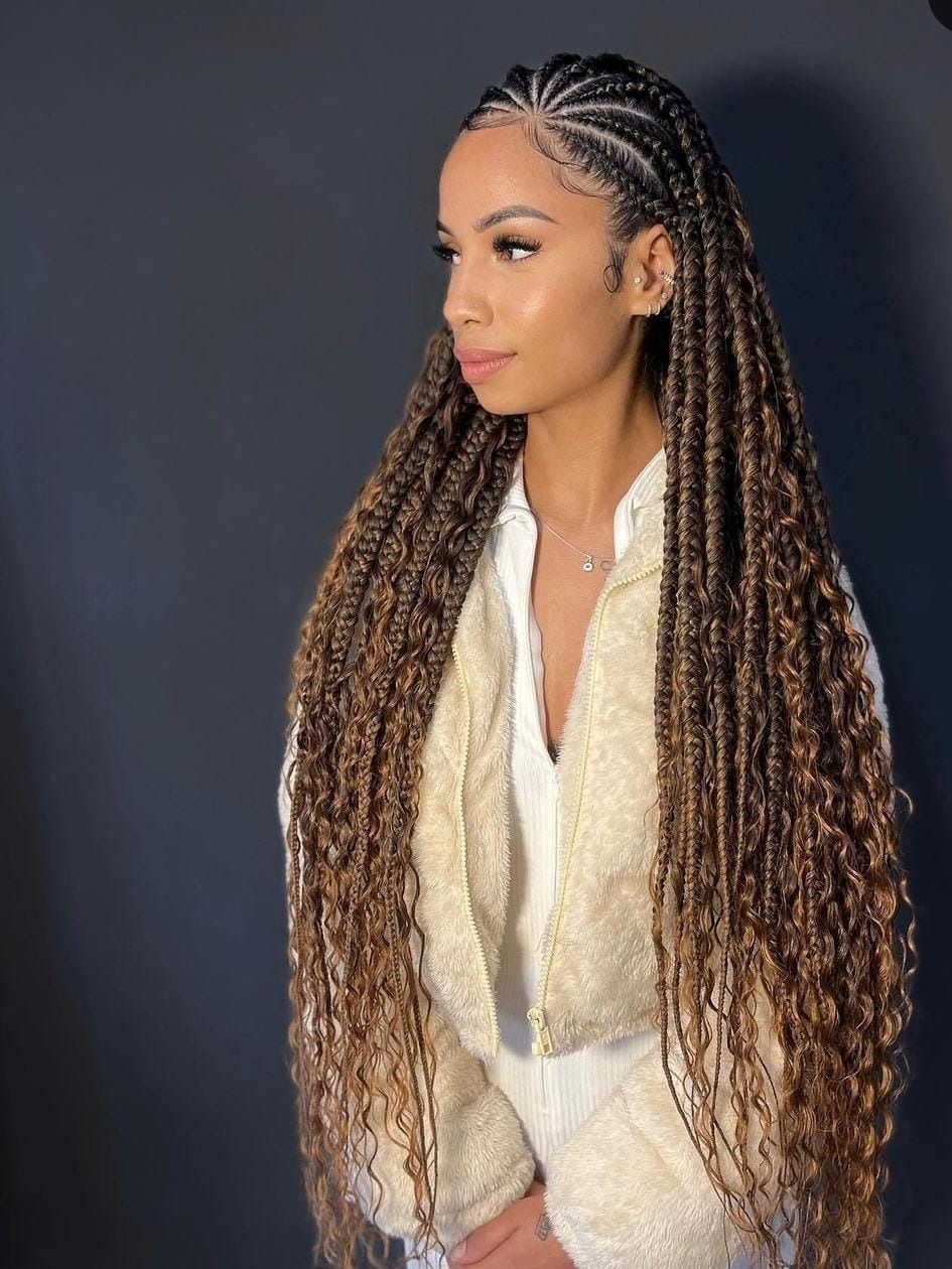 Mujer con cabello largo trenzado, vestida con una chaqueta blanca, de pie frente a un fondo gris oscuro.