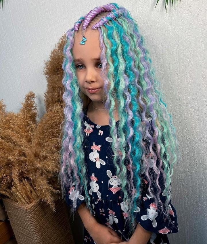 Chica con trenzas largas y rizadas, azules y moradas. Lleva un vestido y un pequeño dije de mariposa en el pelo.