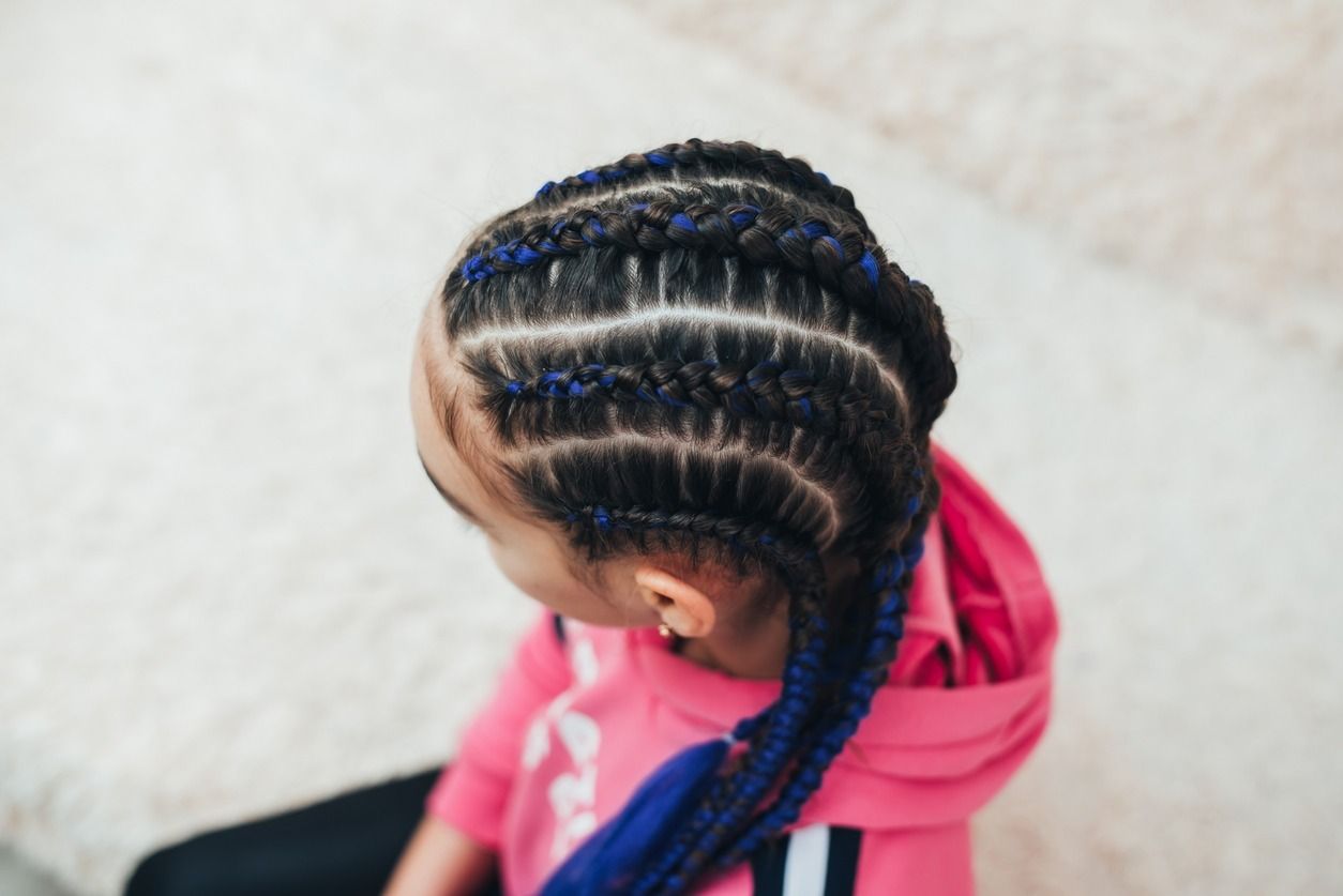 Cabello rubio en trenzas con cuentas, visto desde atrás en un salón con espejo y productos en un estante.