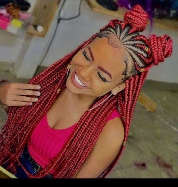 Mujer con trenzas rojas, vistiendo un top rosa, sonriendo con sus manos tocando su cabello.