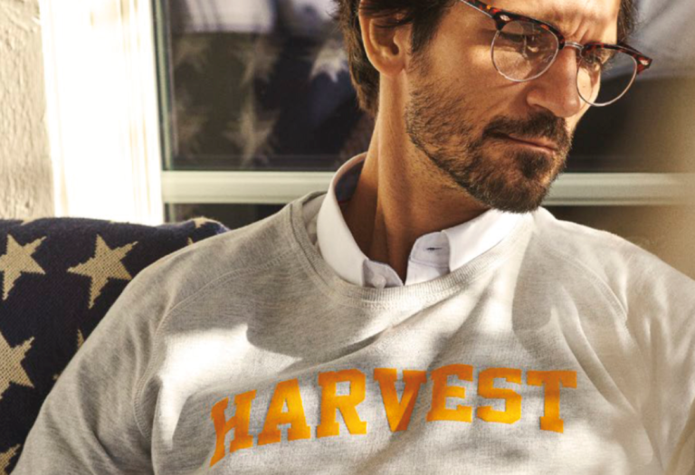 Person mit Bart und Brille trägt über einem weißen Hemd mit Kragen ein graues Sweatshirt mit der Aufschrift „HARVEST“.