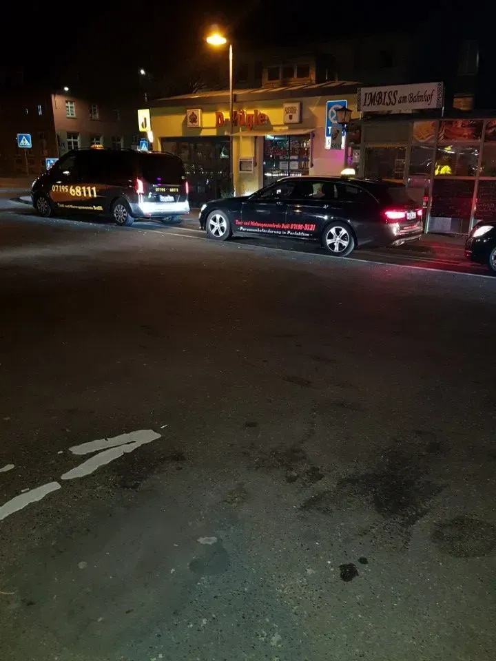 Nächtliche Straßenszene mit geparkten schwarzen Autos vor einem beleuchteten Ladenlokal