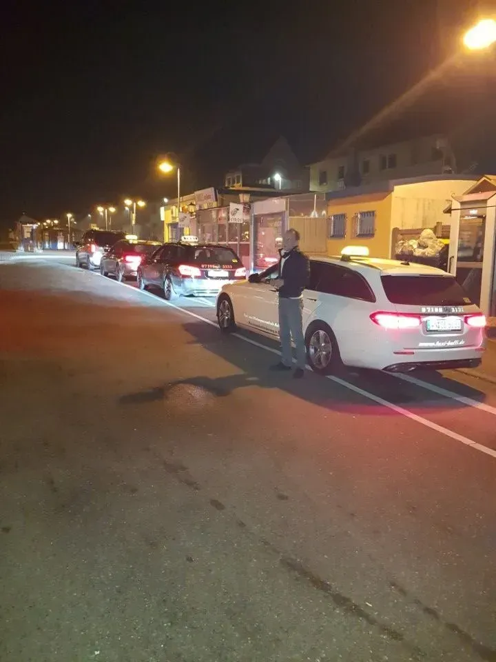 Eine nächtliche Straße mit einer Reihe geparkter Autos und Häusern entlang des Bordsteins, beleuchtet von Straßenlaternen.
