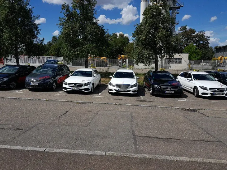 Geparkte Autos entlang einer Straße neben Bäumen und Gebäuden unter einem teilweise bewölkten Himmel