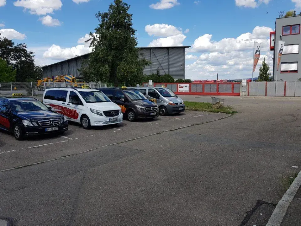 An einem bewölkten Tag parkten Autos neben einem großen Industriegebäude und einem umzäunten Gelände.
