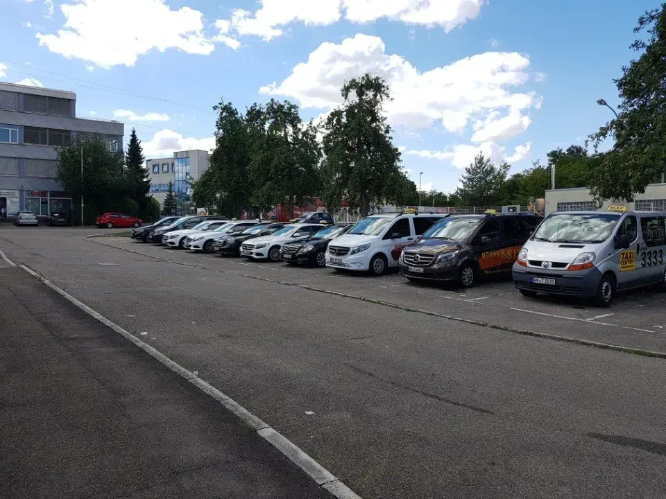Eine Reihe geparkter Autos auf einem Parkplatz neben Gebäuden und Bäumen unter einem bewölkten Himmel