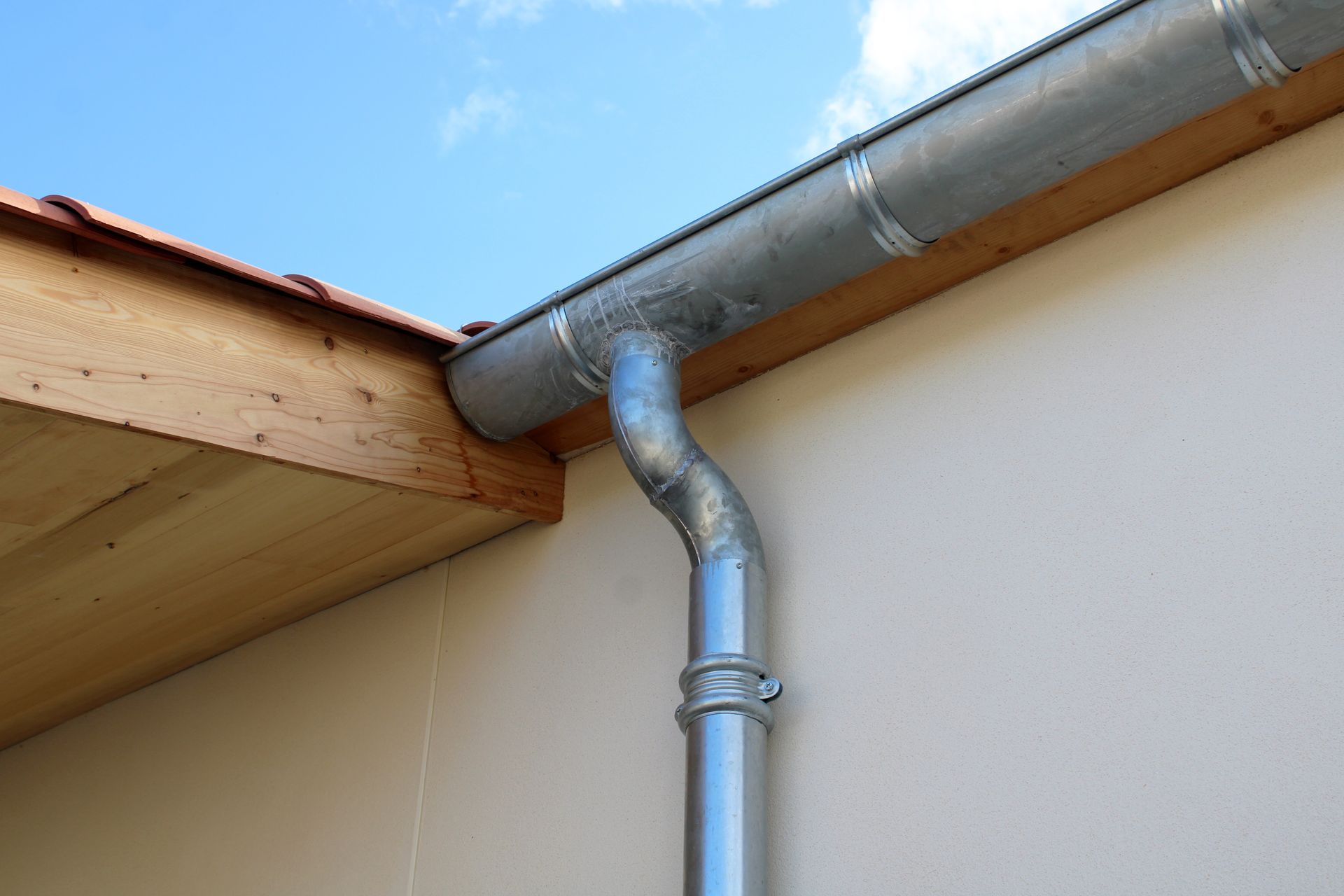 Gouttière et descente pluviale en métal galvanisé sur un mur blanc.