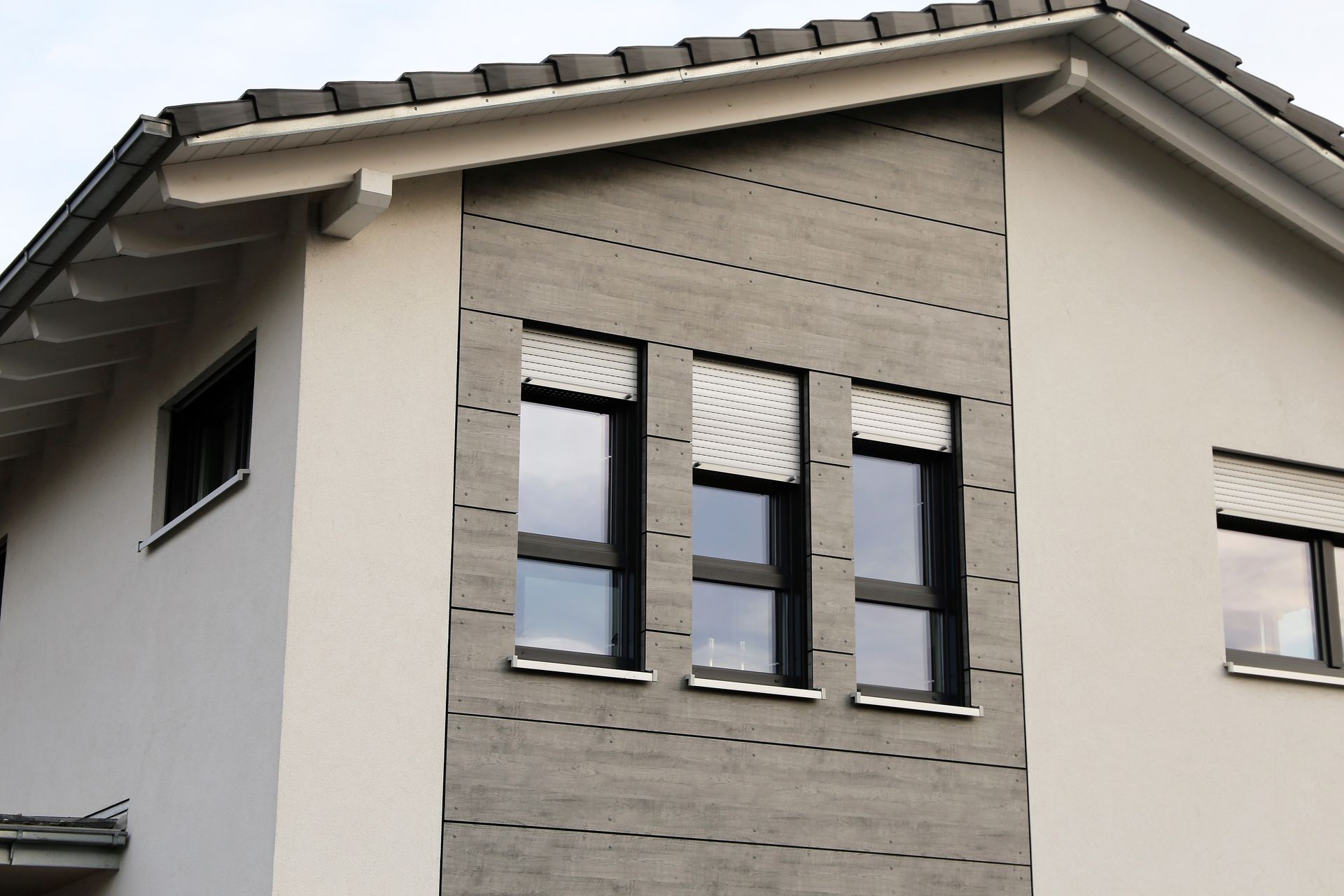Façade de maison gris et blanc avec trois fenêtres verticales.