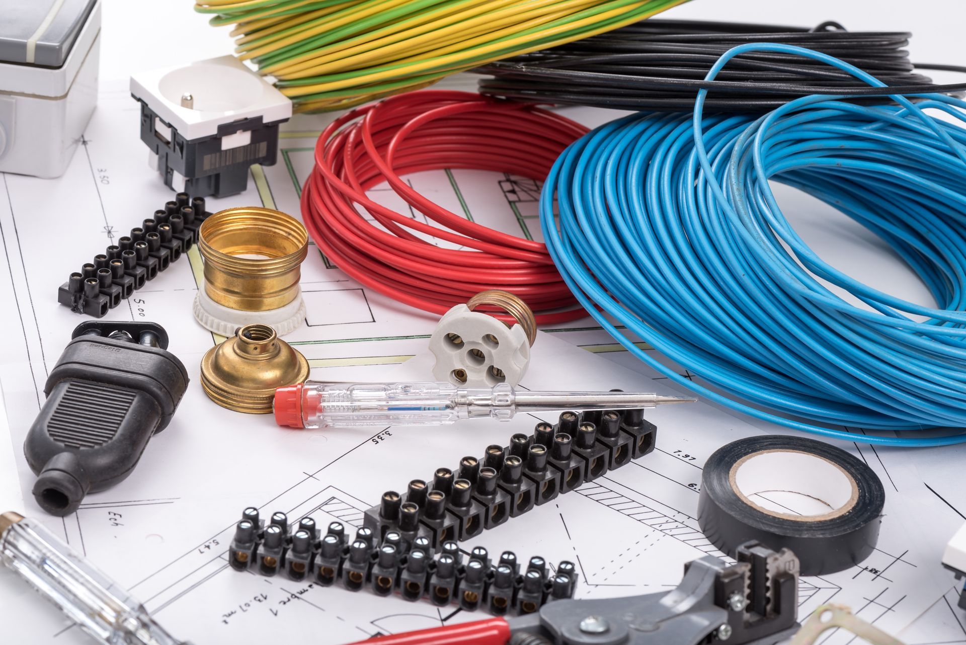 Composants et outils de câblage électrique avec des bobines de câbles rouges, bleus et jaunes sur un établi.