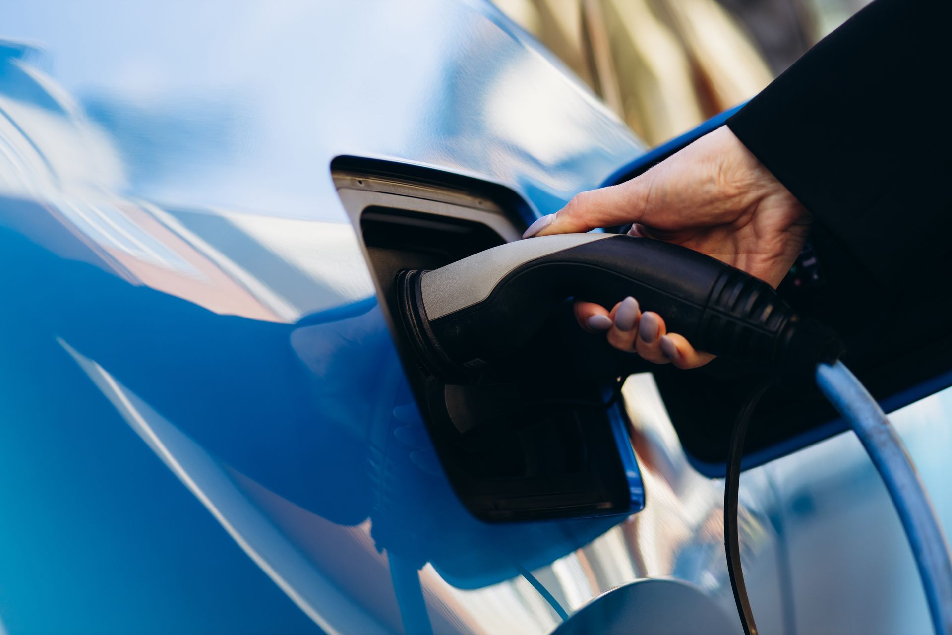 Branchement manuel d'un connecteur de recharge pour véhicule électrique dans une voiture bleue.