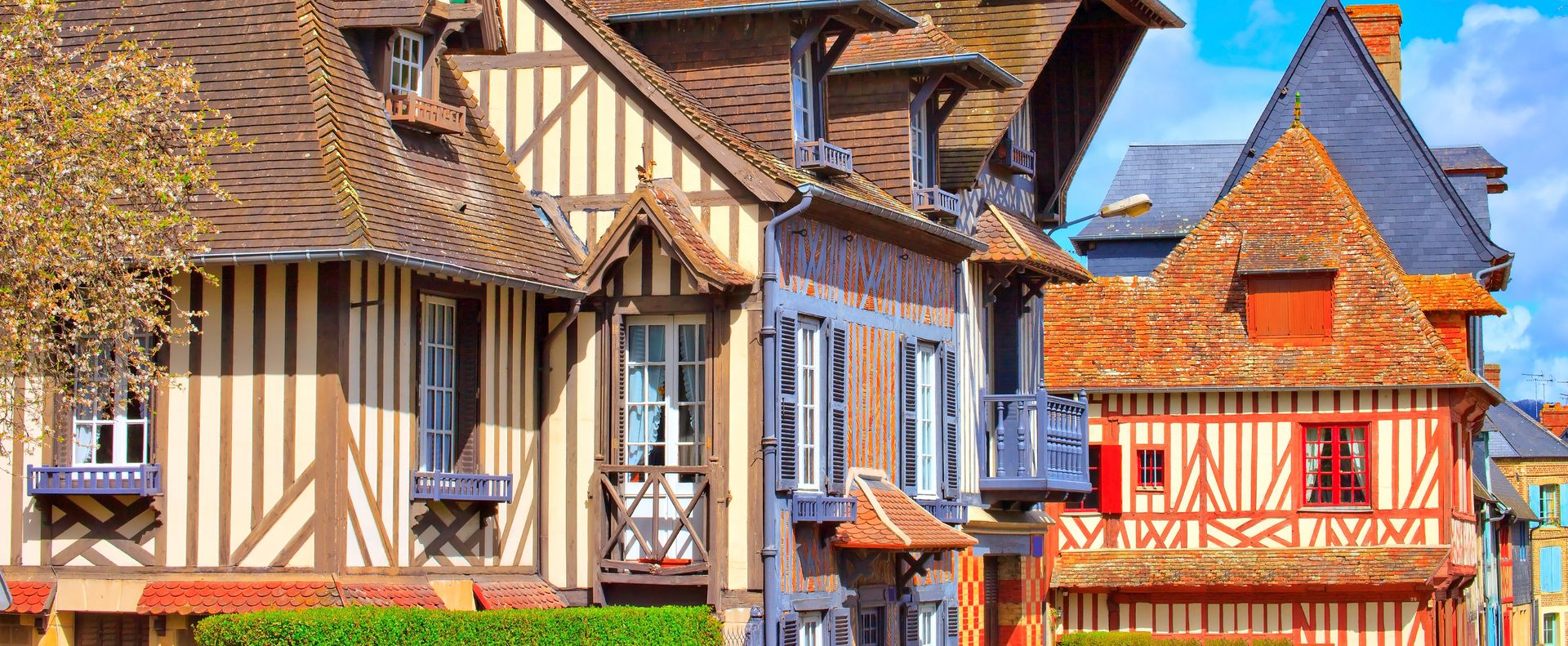 Des maisons à colombages colorées, aux toits pentus et aux façades ornées, dans une rue pittoresque d'un village.