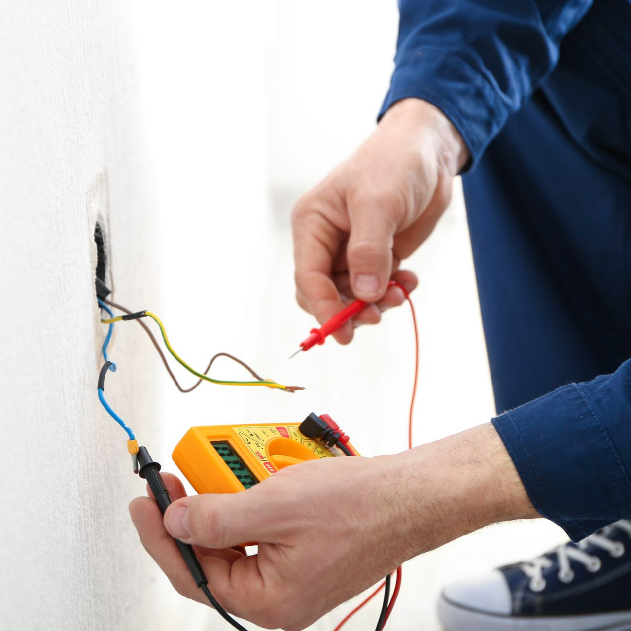 Un électricien teste les câbles muraux exposés à l'aide d'un multimètre et d'une sonde rouge.