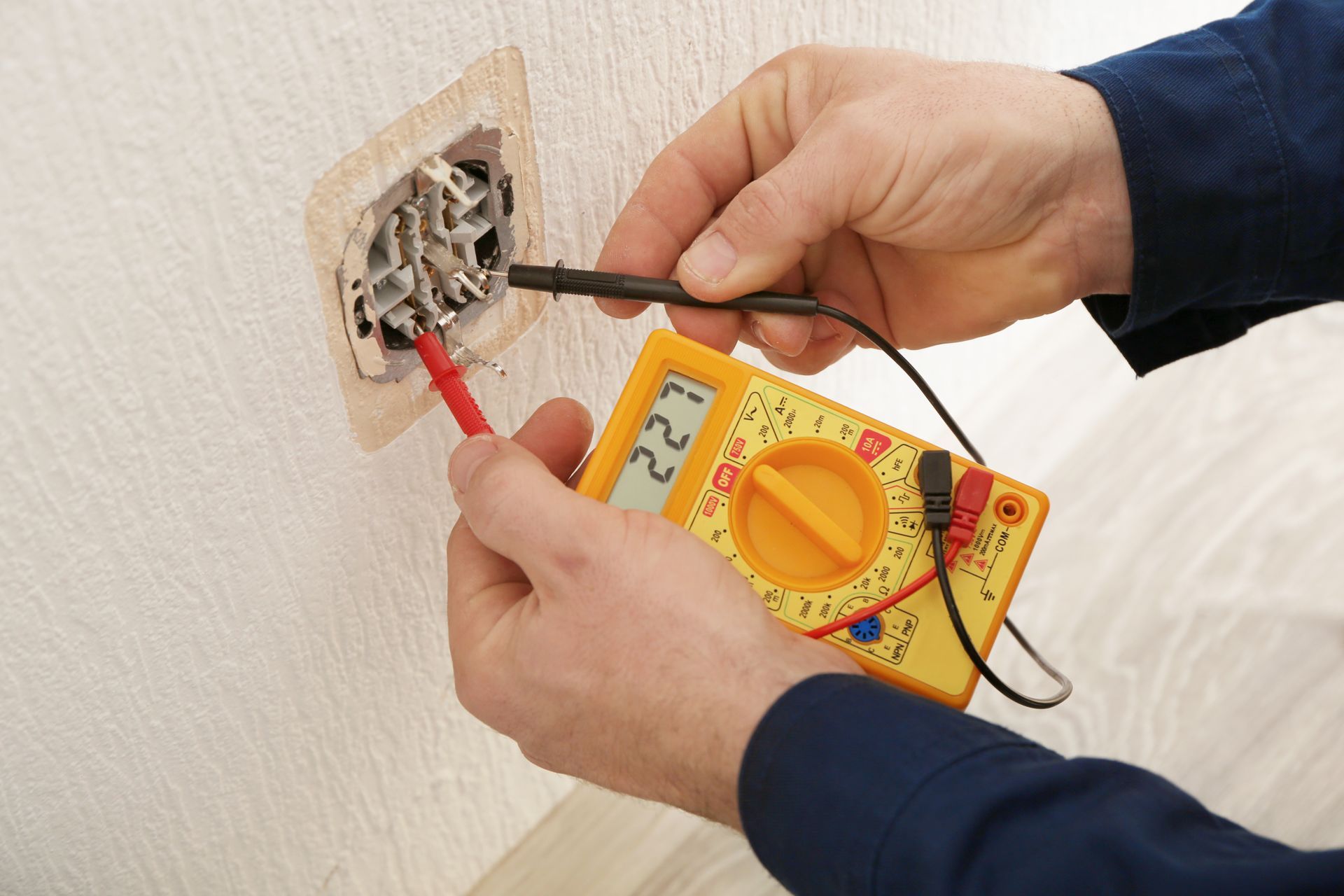 Des mains utilisent un multimètre pour tester le câblage électrique mural avec une boîte de sortie apparente.