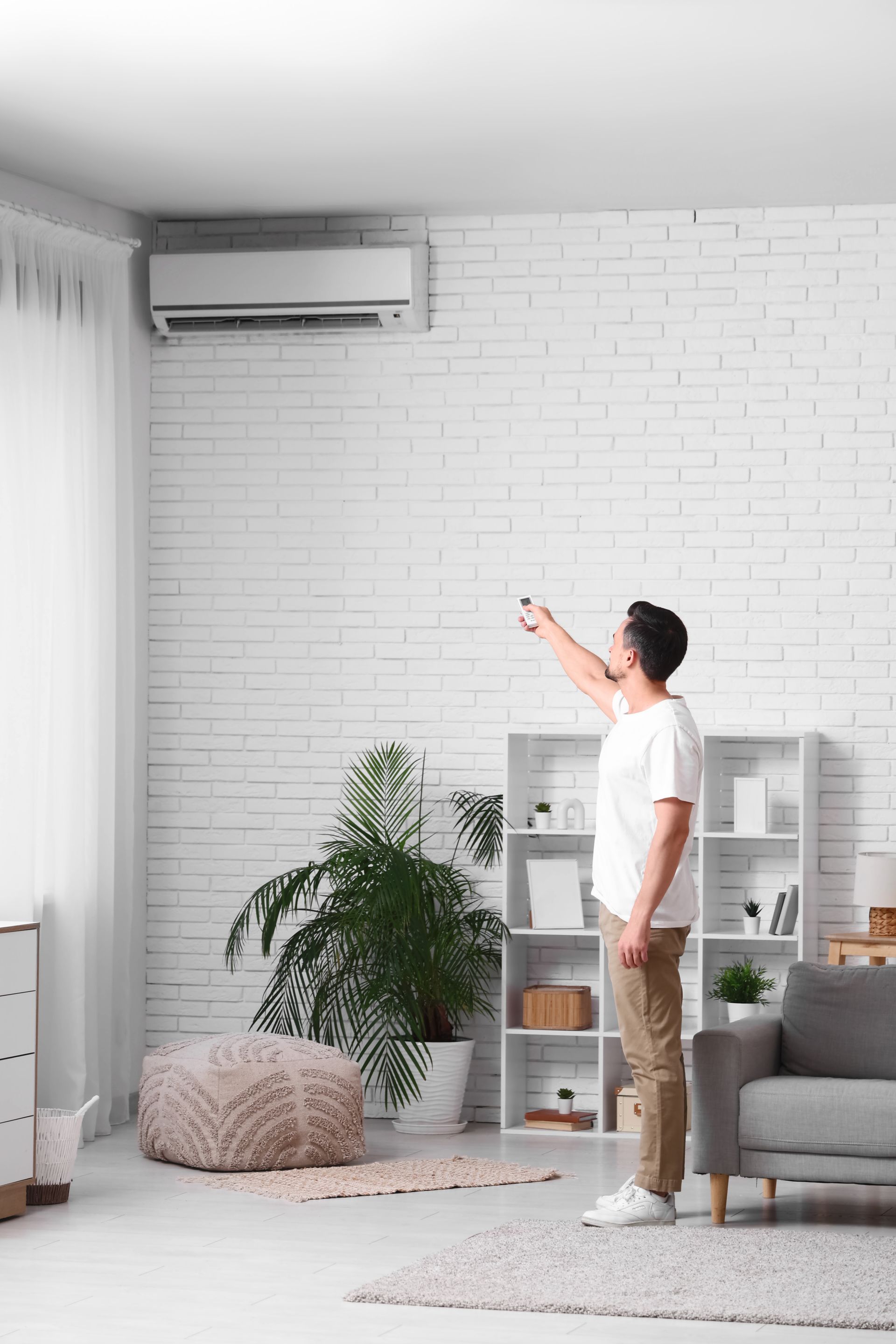 Une personne en chemise blanche désigne du doigt un climatiseur mural dans un salon lumineux.