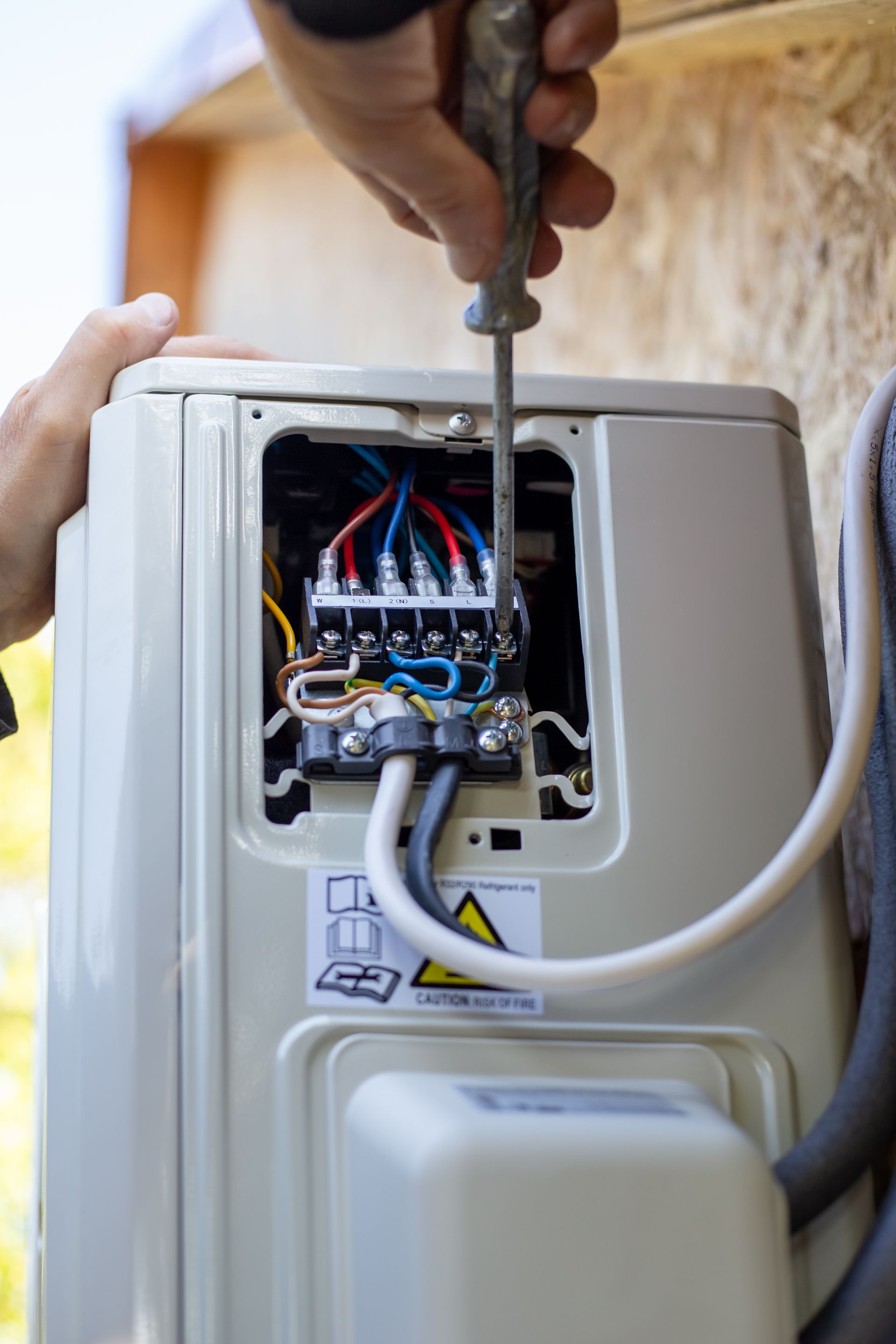 Serrage manuel d'une vis sur un boîtier de commande électrique ouvert avec des fils dénudés.