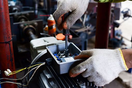 Des mains réparent un petit appareil électronique avec des outils sur un établi dans un atelier.