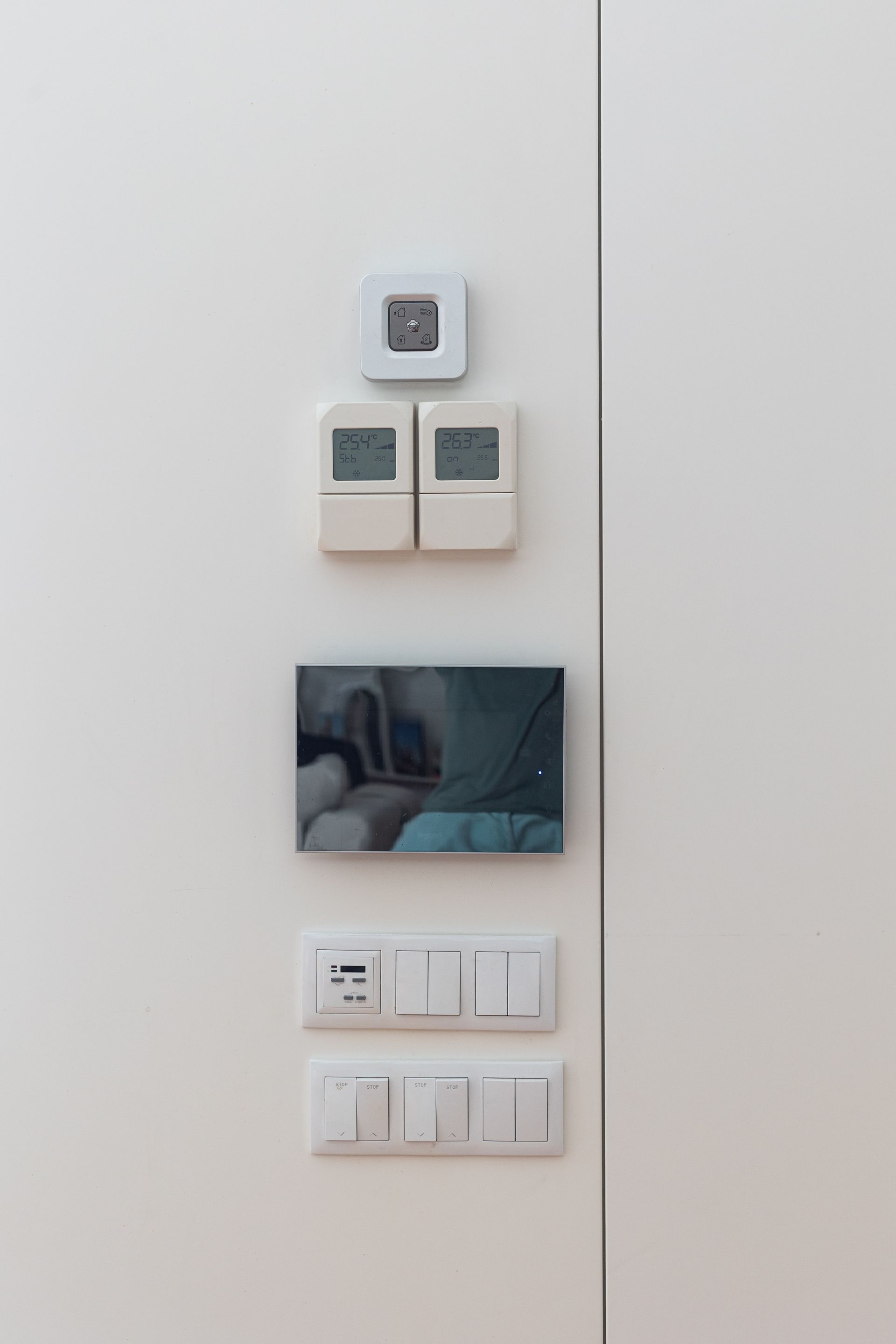Thermostats et interrupteurs muraux à côté d'un petit tableau encadré sur un mur blanc.