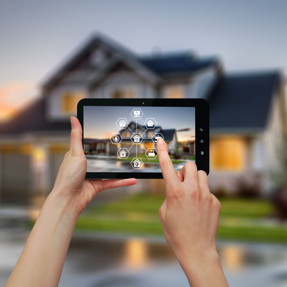 Des mains utilisent une tablette pour contrôler une maison intelligente devant une maison au crépuscule.