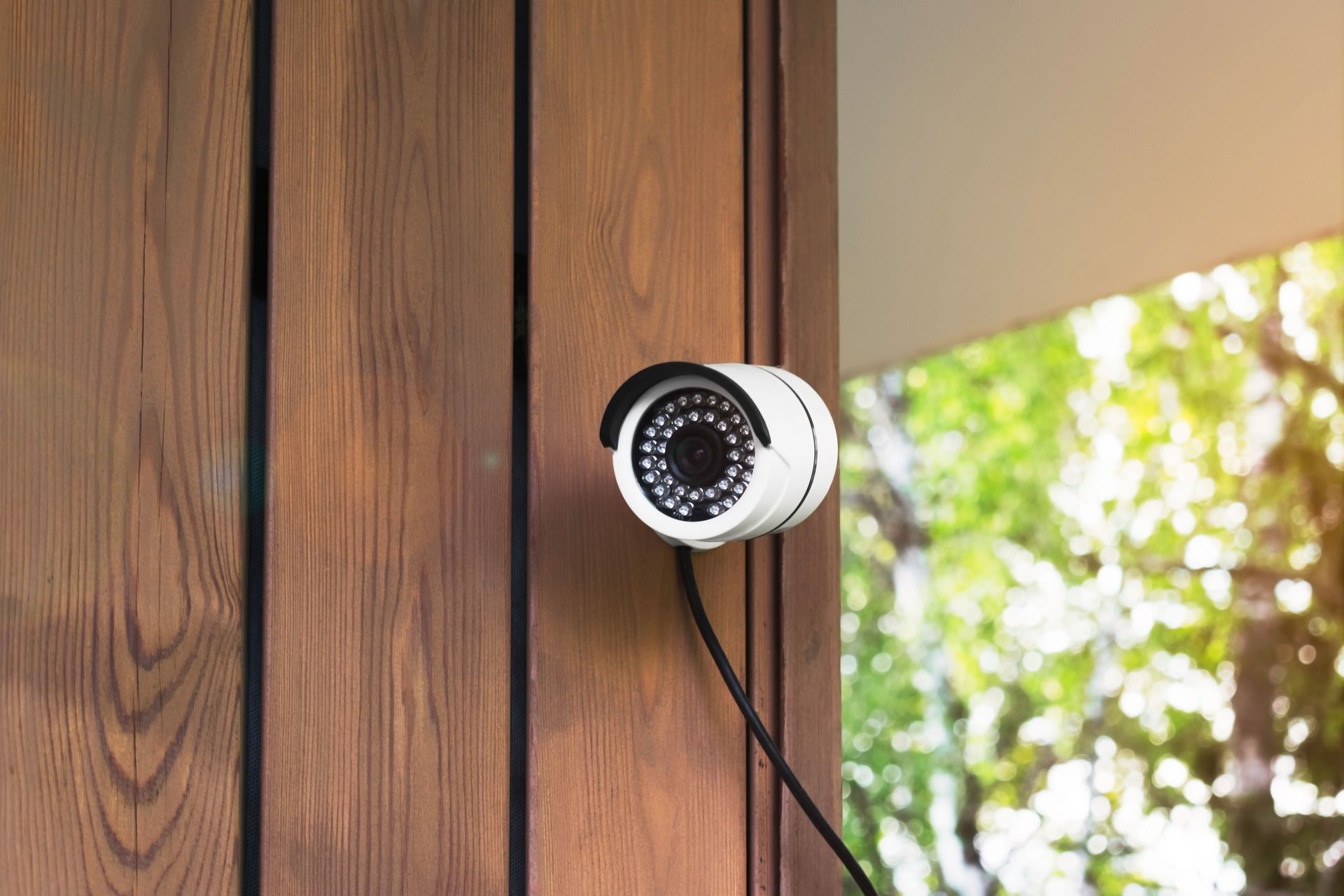 Caméra de sécurité blanche fixée sur un mur en bois, donnant sur une porte extérieure.