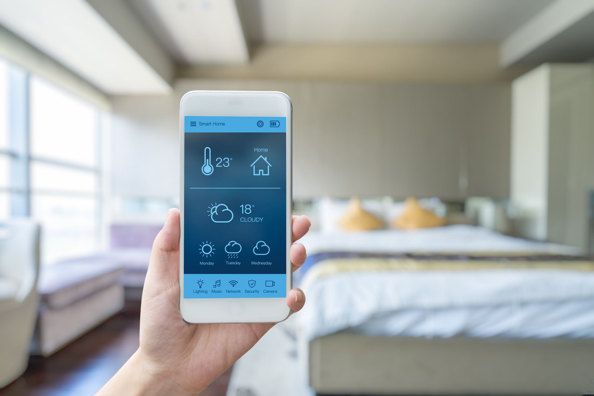 Une main tenant un smartphone montrant une application de pilotage de maison intelligente dans une chambre.