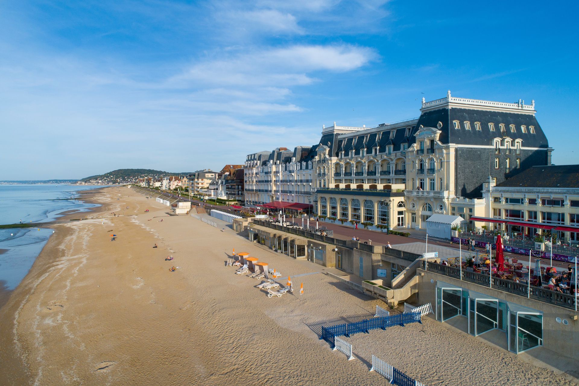 Plage ensoleillée et promenade en bord de mer bordée d'hôtels sous un ciel bleu.