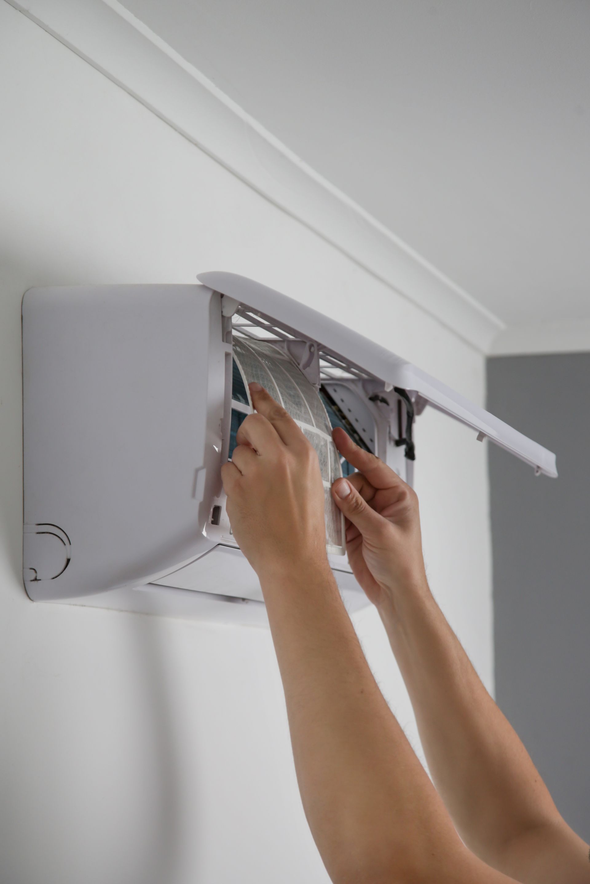 Des mains installent un panneau de climatisation mural blanc à l'intérieur, à l'aide d'outils.