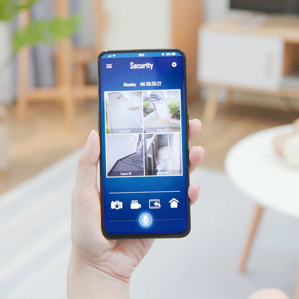 Main tenant un smartphone montrant une application de caméra de sécurité domestique avec quatre flux vidéo en direct.