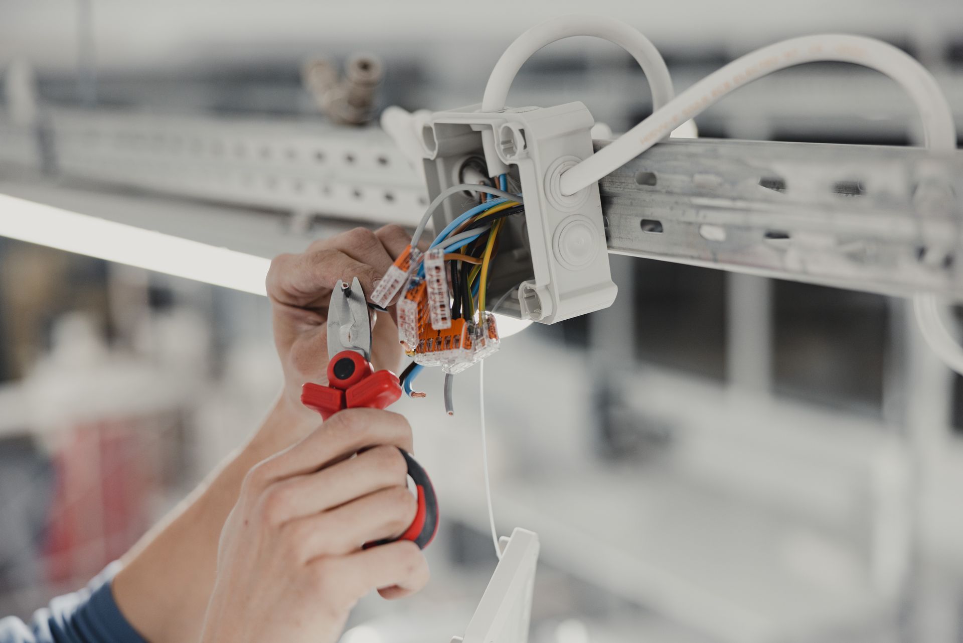 Un technicien effectue le câblage d'un boîtier de commande électrique à l'aide d'une pince à poignée rouge dans un atelier.