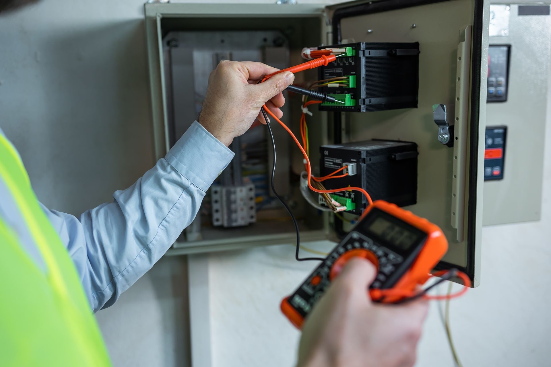 Un technicien utilise un multimètre pour tester le câblage à l'intérieur d'une armoire électrique ouverte.