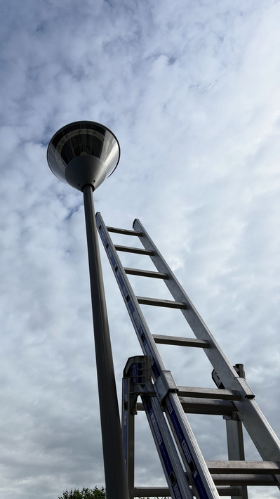 Échelle penchée vers un lampadaire sur fond de ciel nuageux.