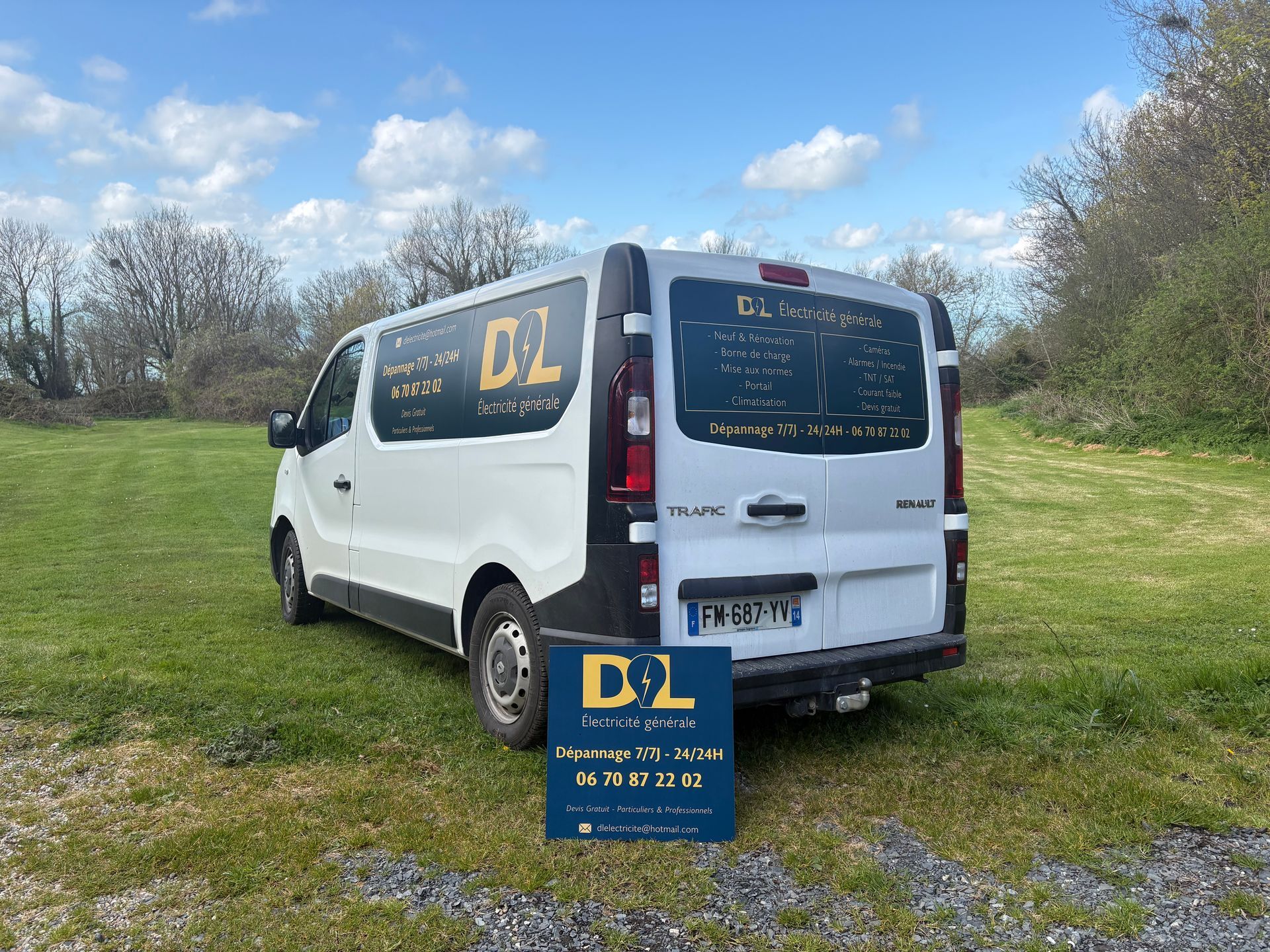 Une camionnette blanche portant l'inscription DL est garée sur l'herbe sous un ciel partiellement nuageux.
