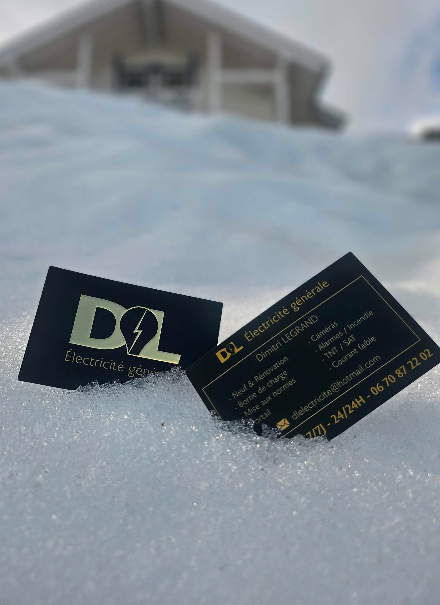 Deux cartes de visite noires sur fond de neige, avec une maison floue en arrière-plan.