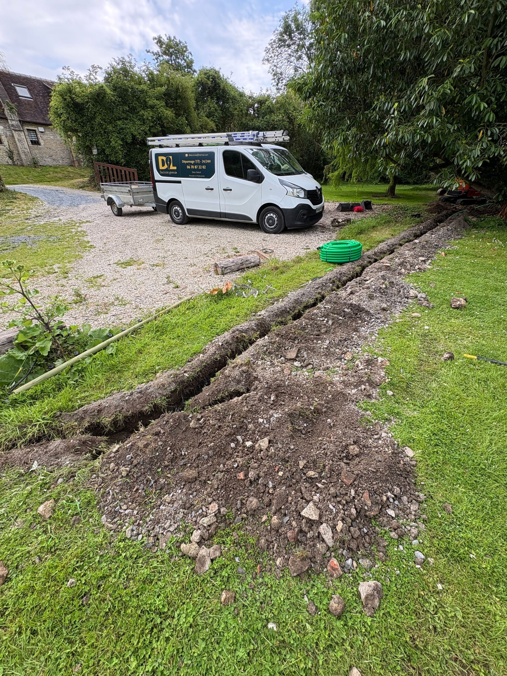 Une camionnette blanche est garée sur du gravier à côté d'une longue tranchée creusée dans une cour herbeuse.