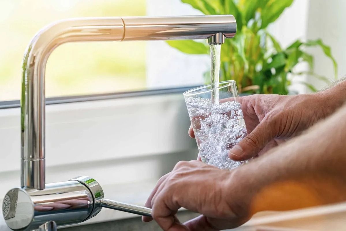 Eine Person gießt aus einem Wasserhahn Wasser in ein Glas.