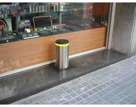 Un bote de basura de acero inoxidable está en la acera frente a una tienda.
