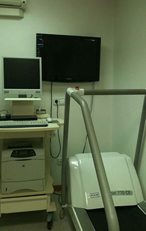Hay una cinta de correr en una habitación al lado de una computadora y una impresora.