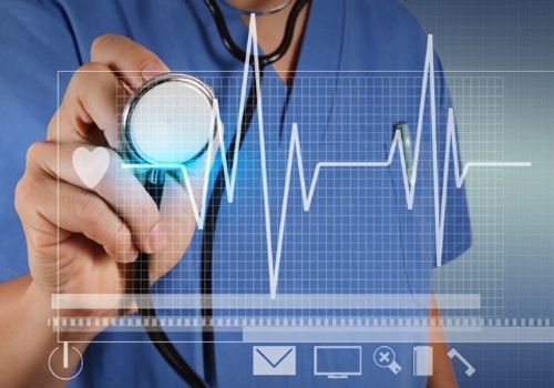 Un médico sostiene un estetoscopio frente a un gráfico de latidos del corazón.