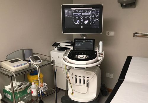 Una máquina de ultrasonido está en una habitación al lado de una mesa de examen.