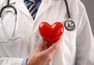Un médico sostiene un corazón rojo delante de su pecho.