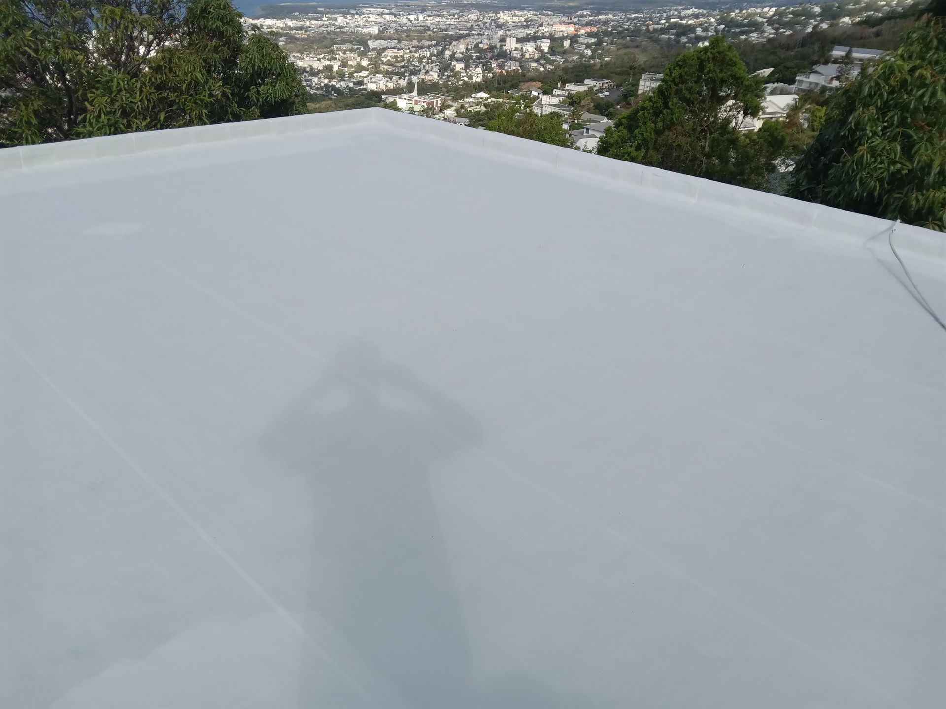 Un toit plat et clair, avec une vue sur la ville en arrière-plan. L'ombre d'une personne se projette sur le toit.