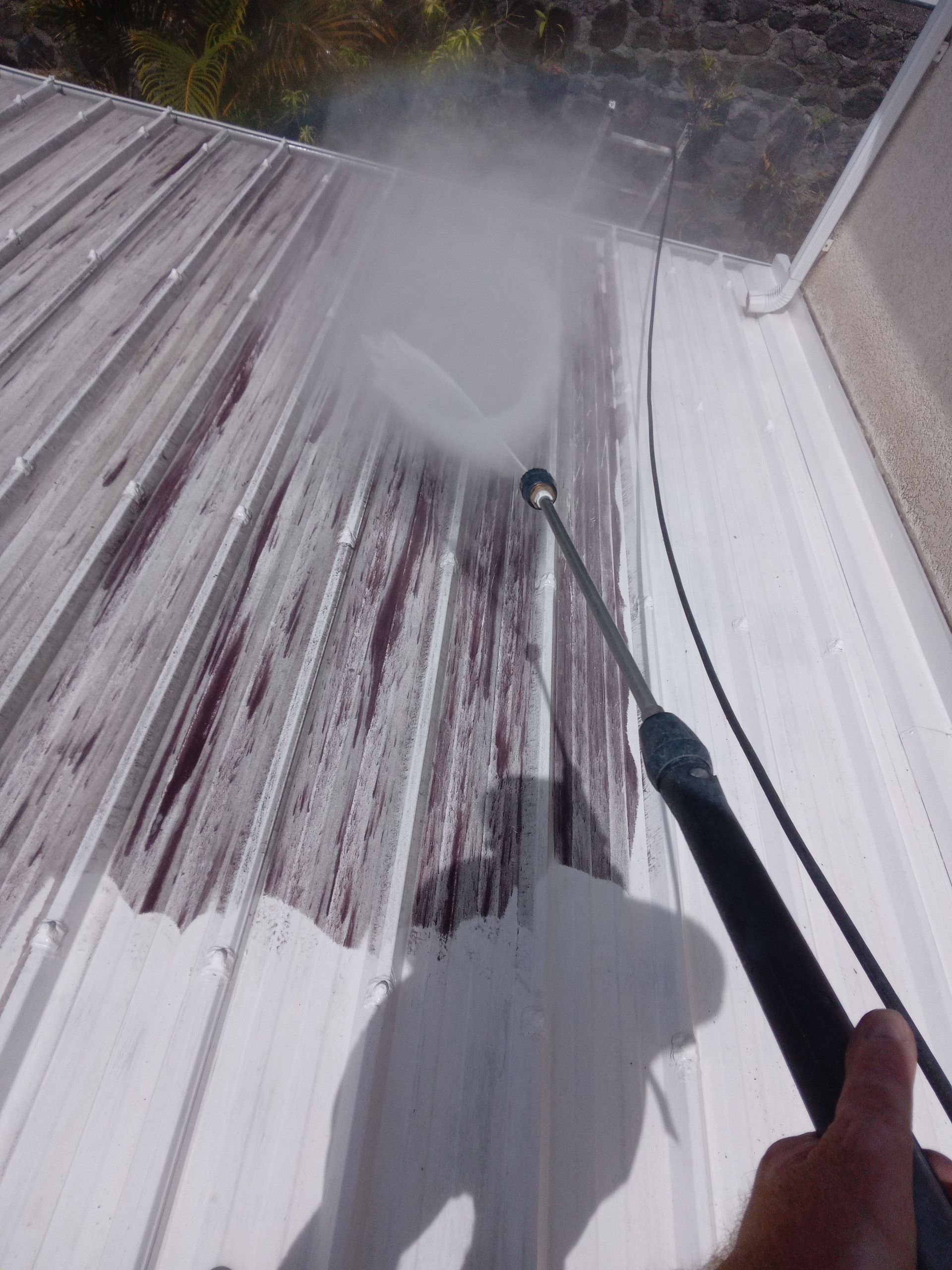 Nettoyage à haute pression d'un toit en métal blanc taché de rouge.