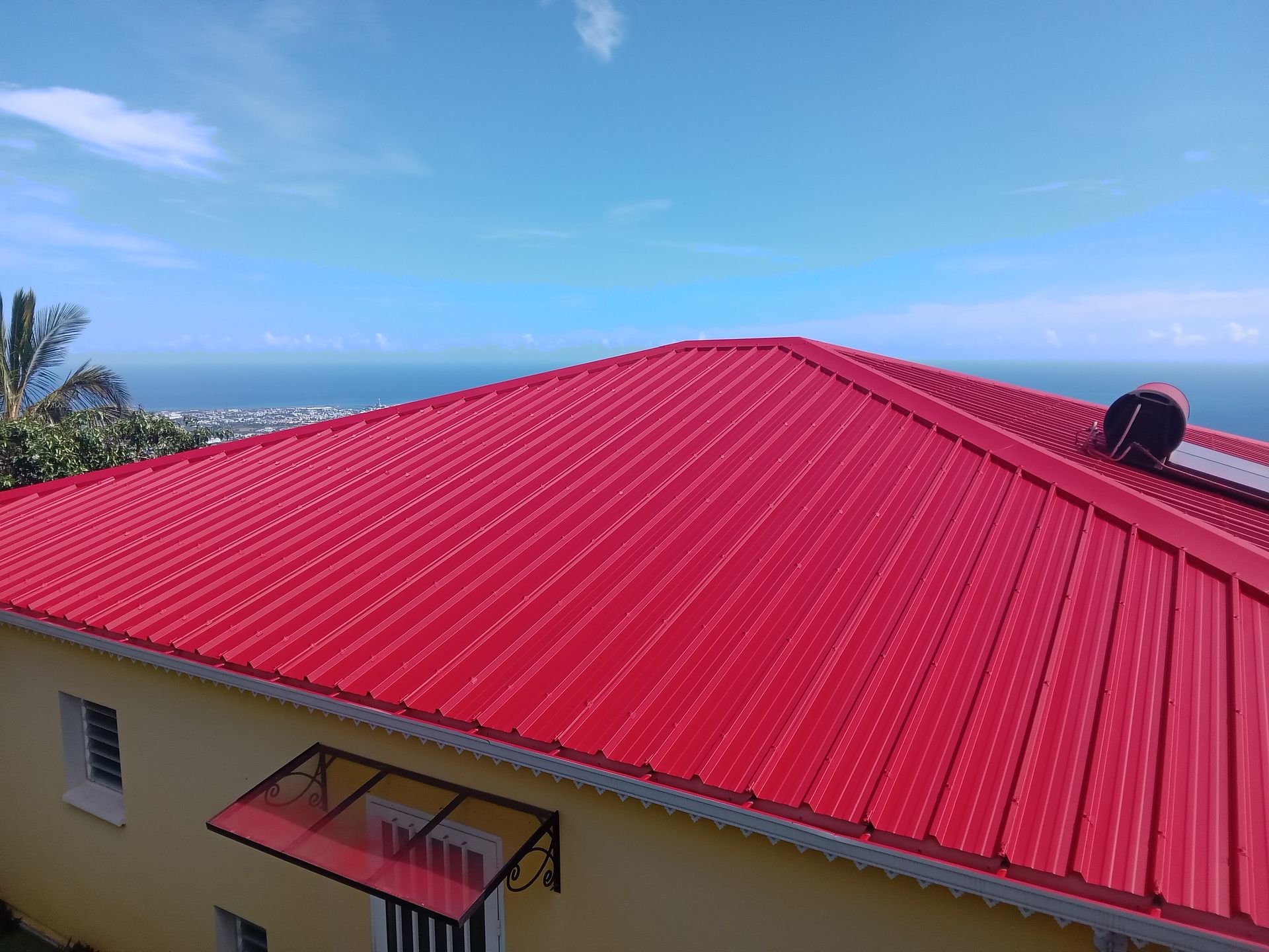 Toit en tôle ondulée rouge sur un bâtiment jaune sous un ciel bleu avec vue sur l'océan.