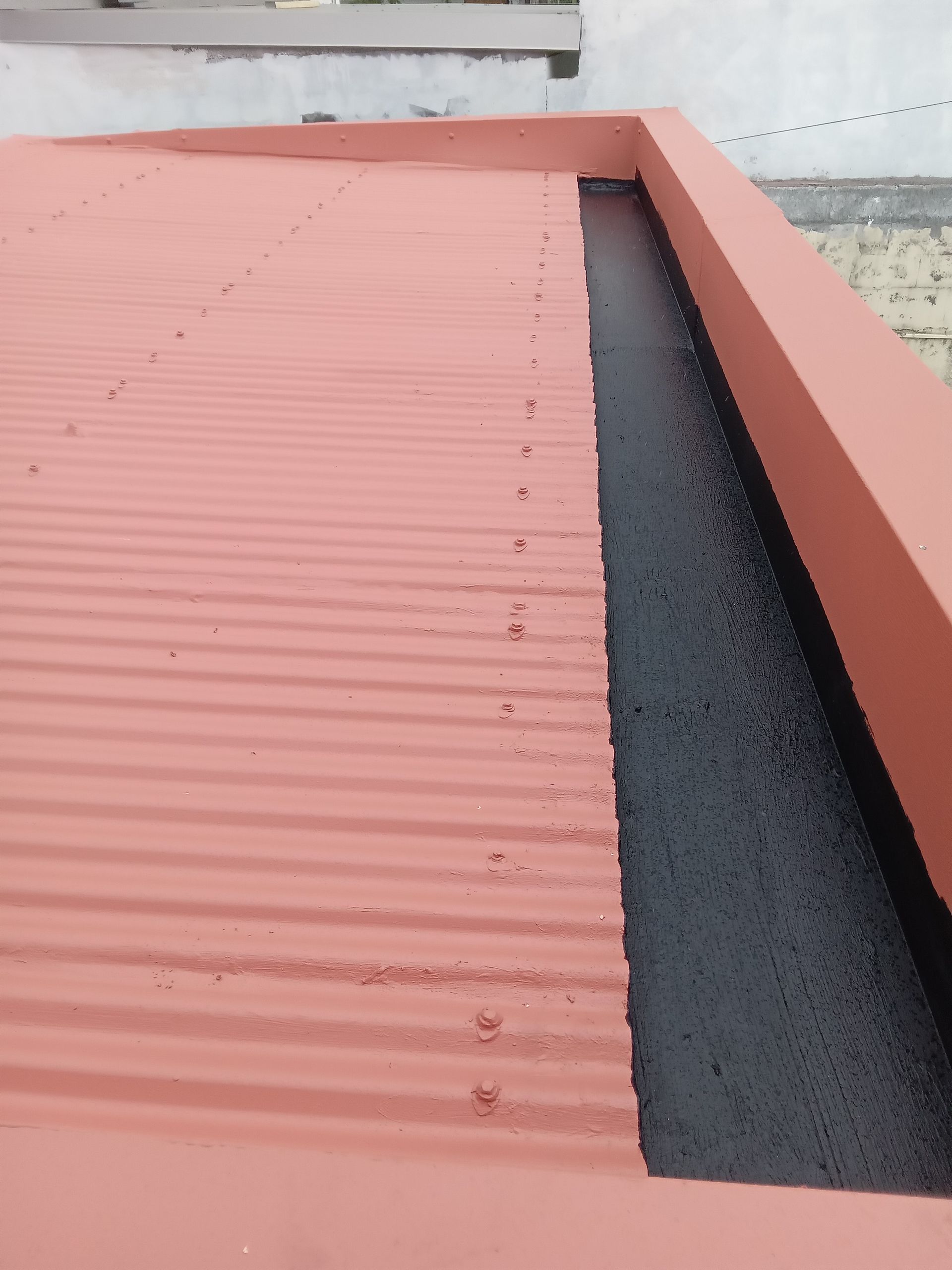 Toit en tôle ondulée rouge avec gouttière noire.