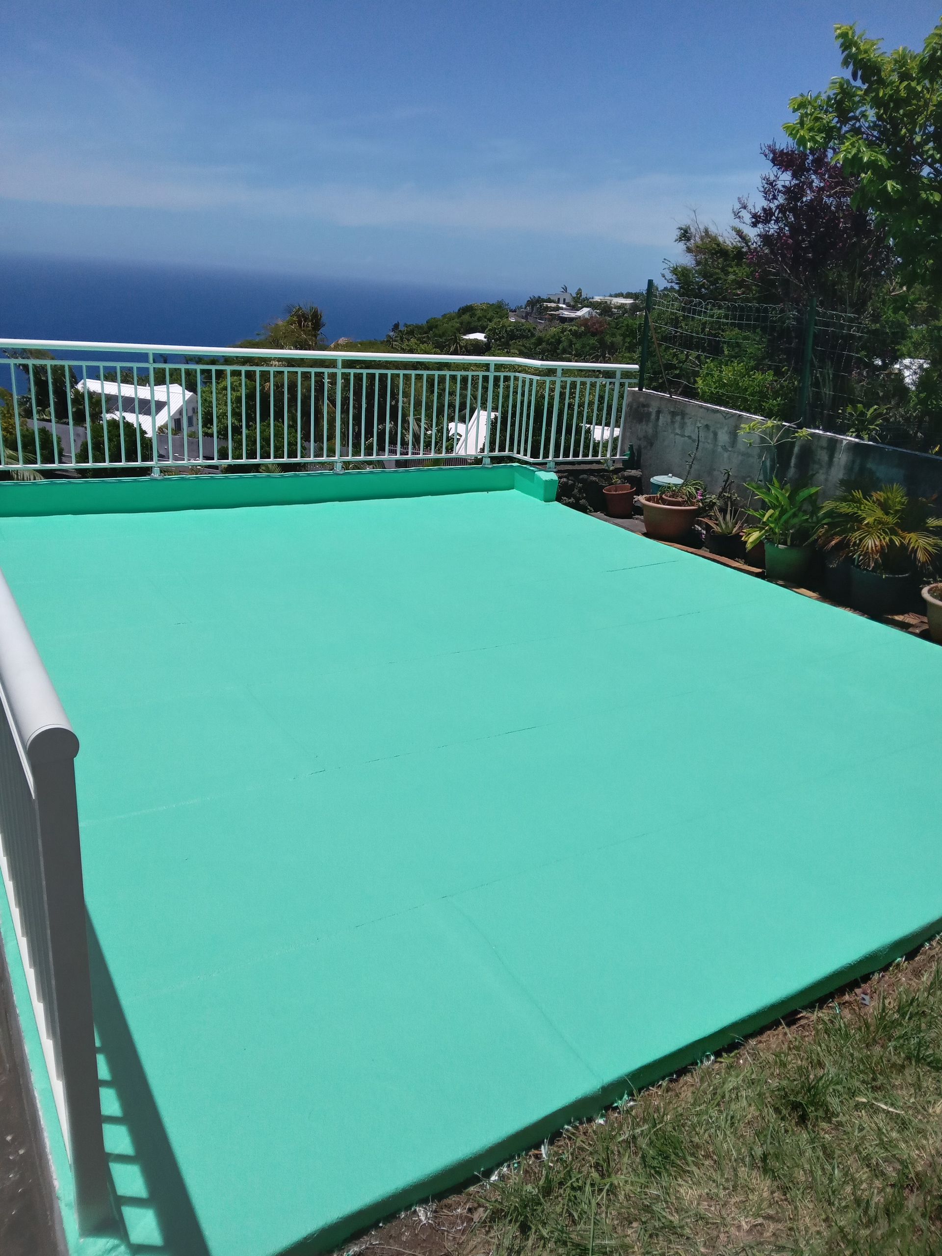 Terrasse sur le toit peinte en vert avec une balustrade blanche, donnant sur l'océan et la ville au loin.