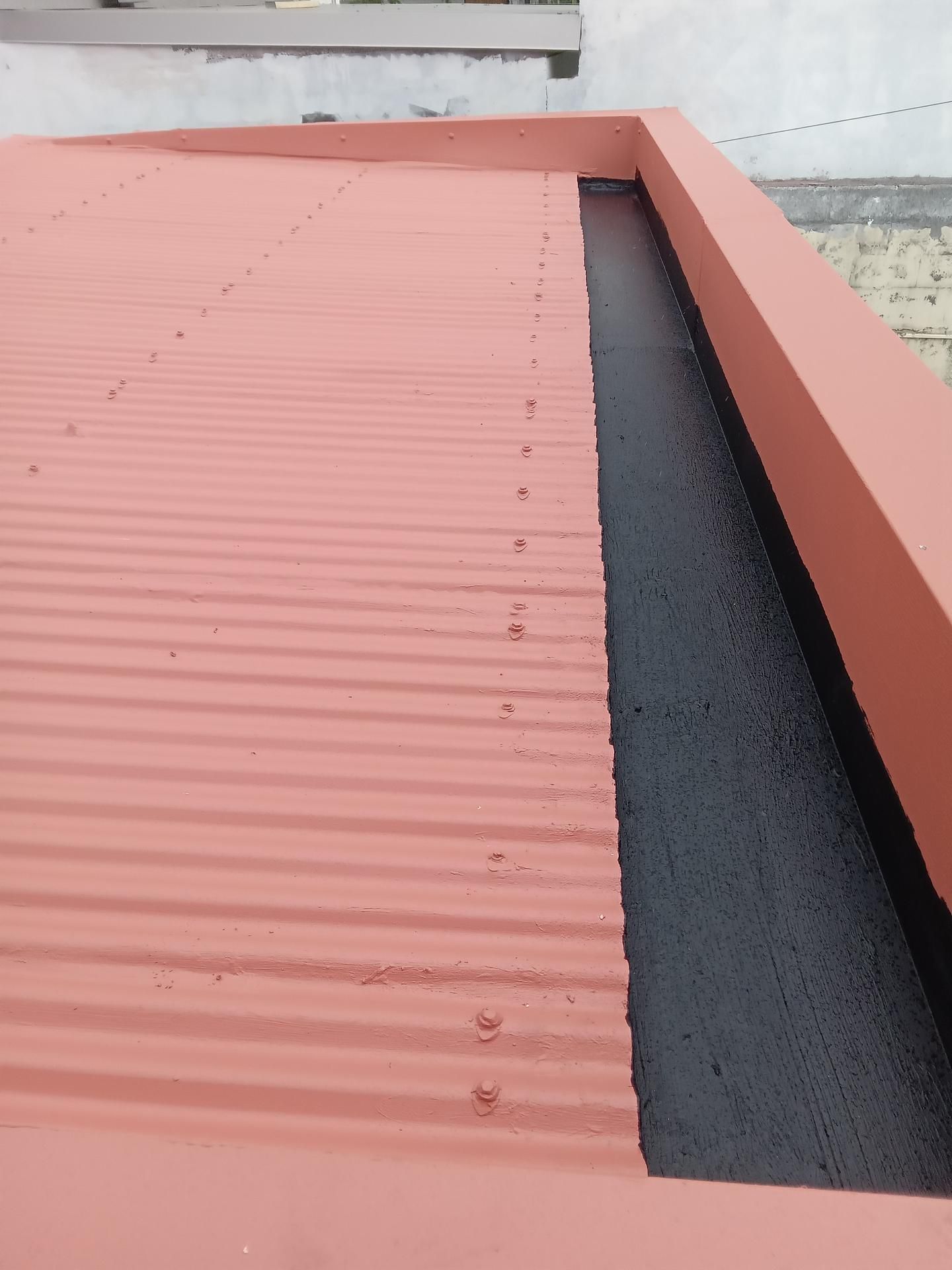 Toit en tôle ondulée rouge avec gouttière noire.