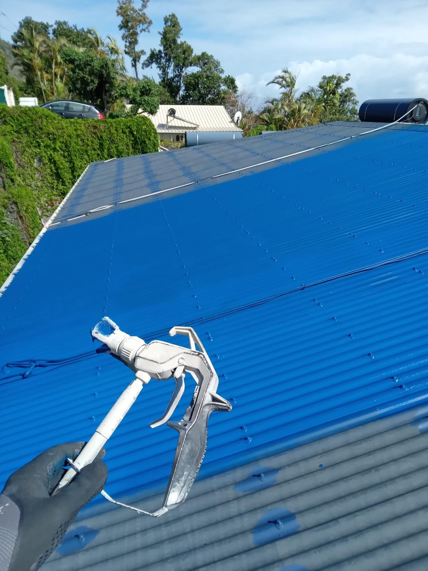 Une personne pulvérise de la peinture bleue sur un toit en tôle ondulée.