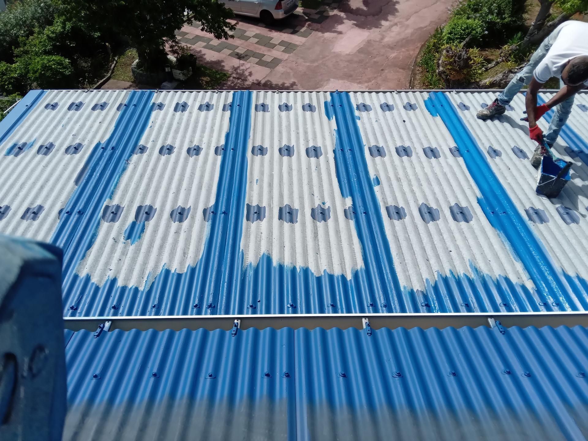 Une personne peignant en bleu un toit en tôle ondulée.